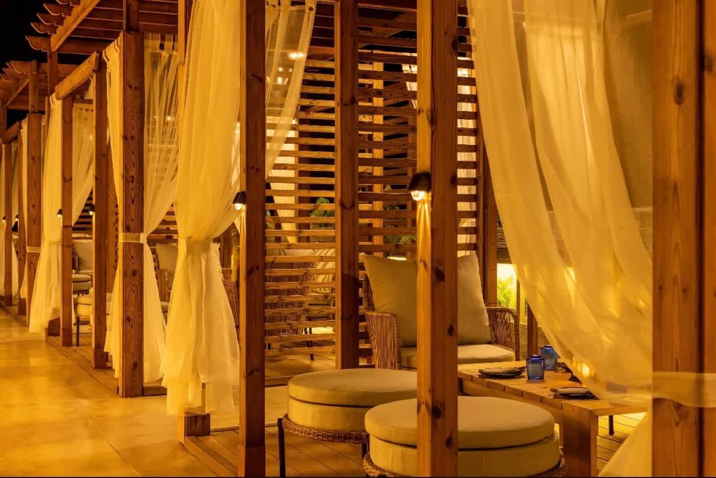 Wooden cabanas with sheer curtains glowing at night